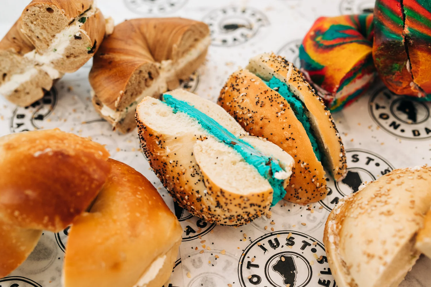 An assortment of Not Just Bagels bagels with cream cheese on branded paper